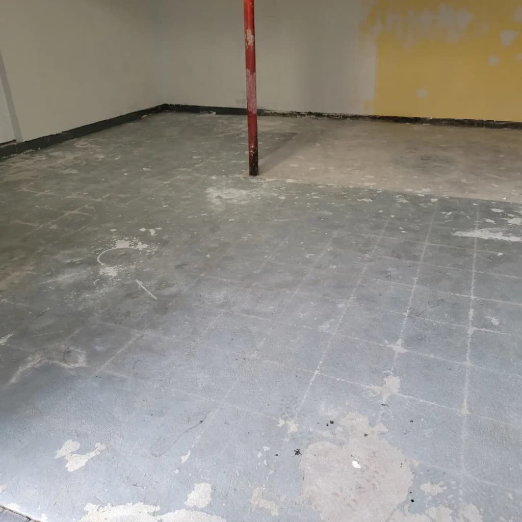 Basement floor with old tile adhesive residue and deteriorated surface before epoxy