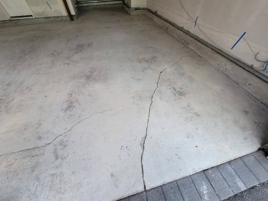 Garage concrete floor with large cracks and oil stains before epoxy